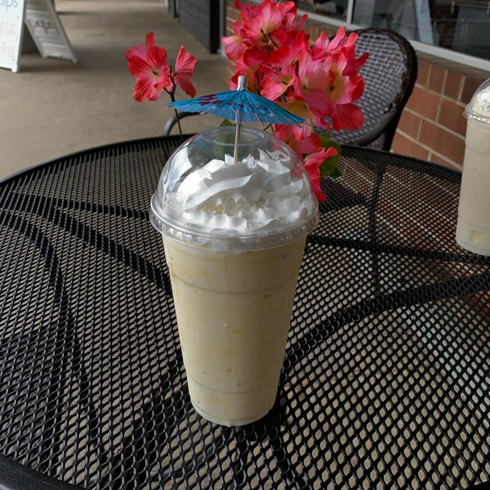 A Capri's Pizzeria milkshake with whipped cream and a blue umbrella on an outdoor table.