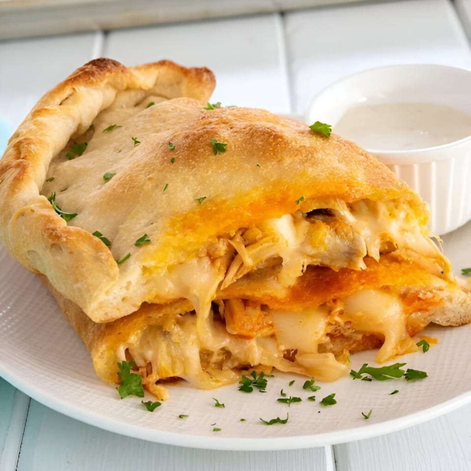 Golden-brown calzone filled with melted cheese and shredded chicken, served with a side of white sauce.