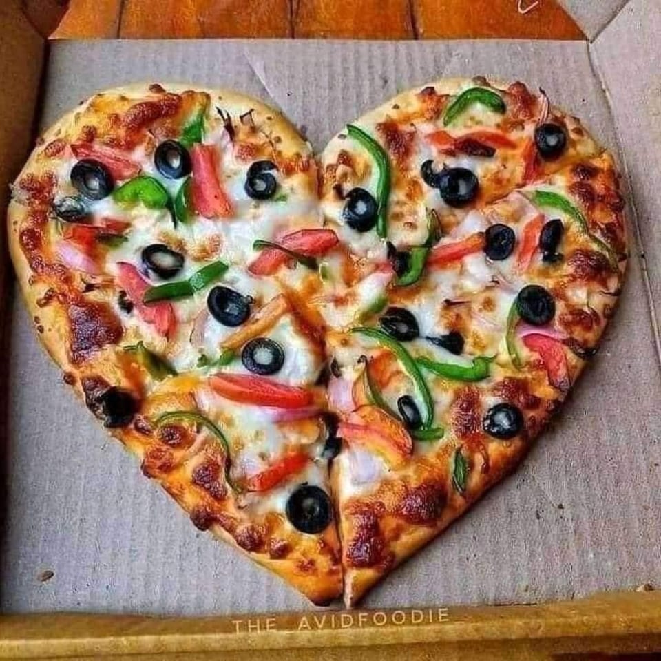 Heart-shaped pizza with black olives, green peppers, and red tomatoes in a Capri's Pizzeria box.