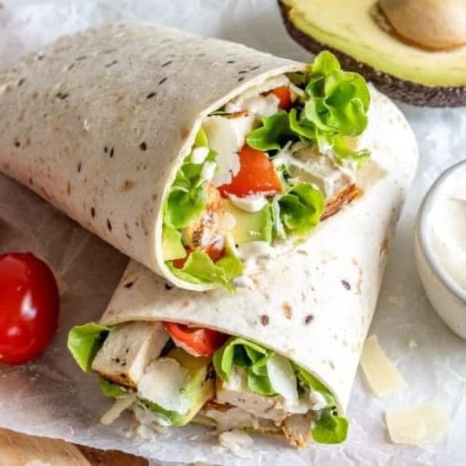 Two chicken wraps filled with lettuce, tomatoes, and cheese, with avocado and cherry tomato.